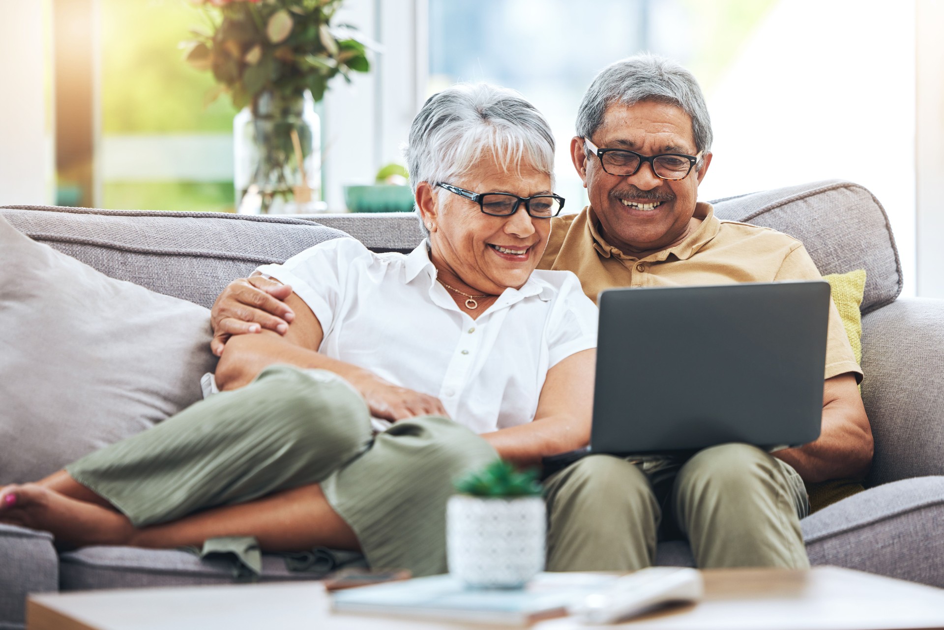 Laptop, happy and senior couple on sofa for watching movies, entertainment and streaming in living room. Retirement, love and man and woman relax on computer for internet, website and online at home